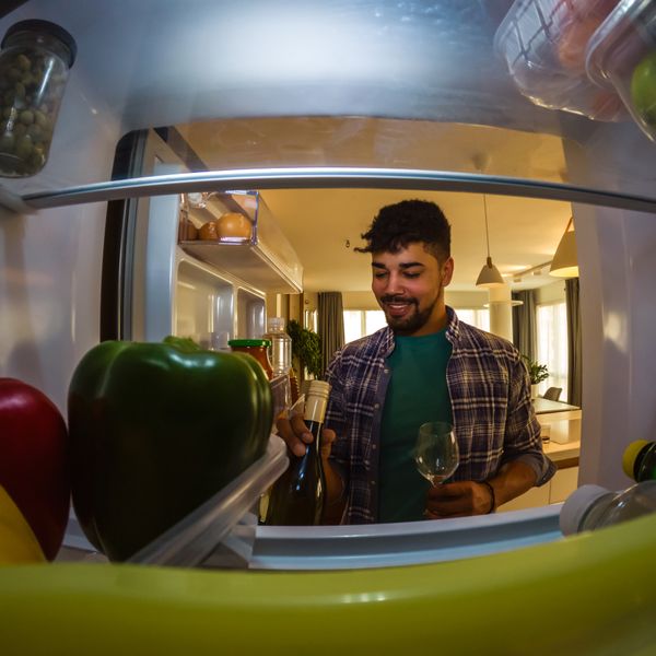 POV of a smiling man grabbing a wine bottle from a fridge 
