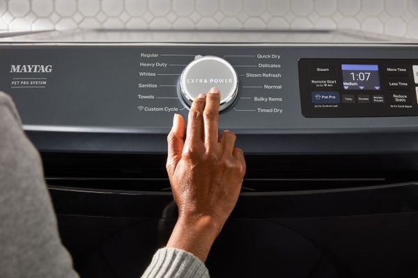 A close-up of a person pressing the Extra button on a Maytag dryer 
