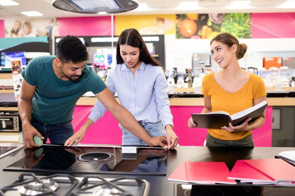 A man and a woman measuring a cooktop while a saleswoman smiles 