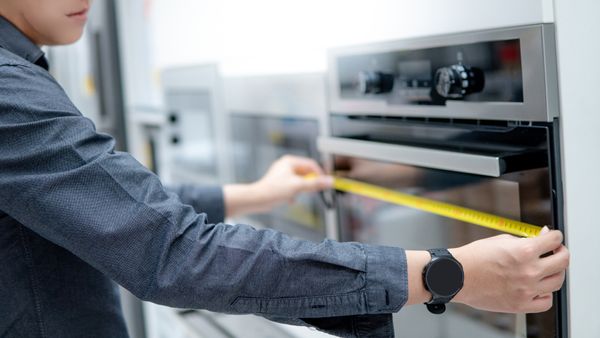 A man using a measuring tape to measure an oven 