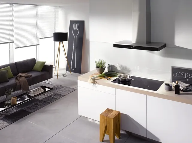 front view of a modern open concept living room and kitchen with the kitchen in the foreground and a Miele induction cooktop built in