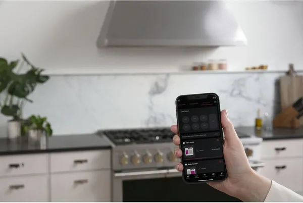 A person holding a smartphone with the Monogram ZDP484NGTSS range in the background 