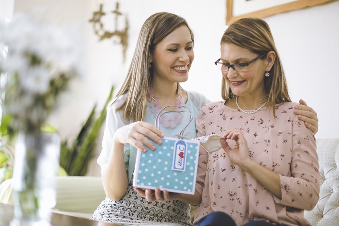 Daughter with arm around mother handing over gift.