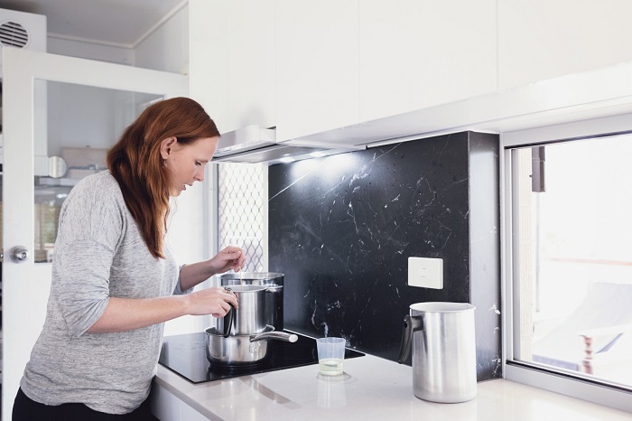 Woman standing over a stove range preparing to make a wax candle.