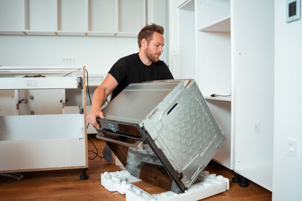 A man mounting a new oven into a cutout 