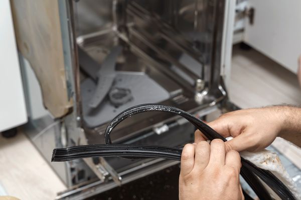 A repair technician removing an old dishwasher gasket 