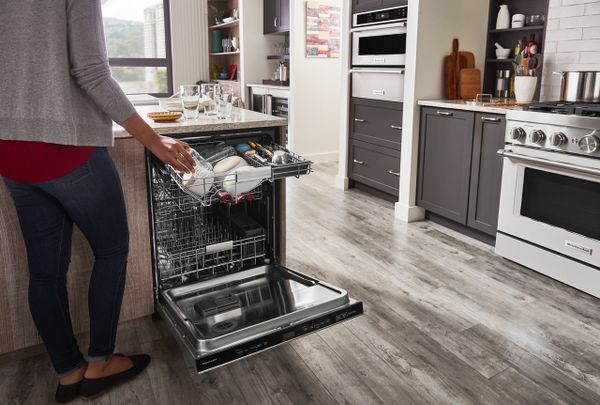 A woman loading dishes into an open KitchenAid KDPM604KPS dishwasher