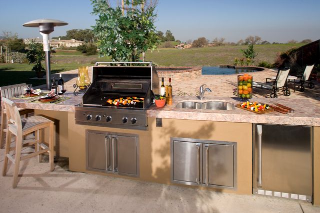 Front view of a modern outdoor kitchen with a stainless steel grill, outdoor sink and fridge, and cabinetry