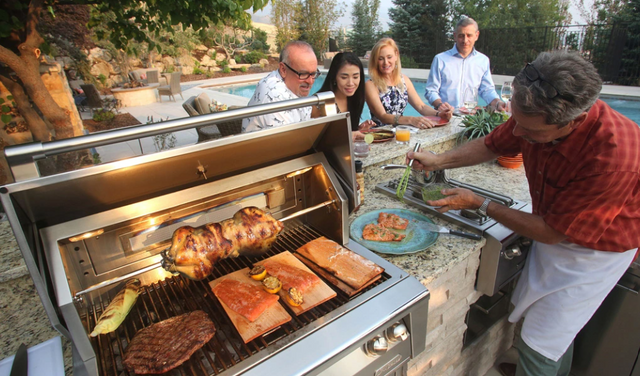 View of a man cooking for a small group of people on an Alfresco grill on an outdoor patio next to a pool