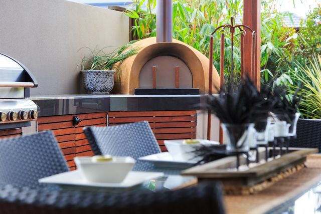 Front view of a modern backyard eating area with a grill and outdoor pizza oven