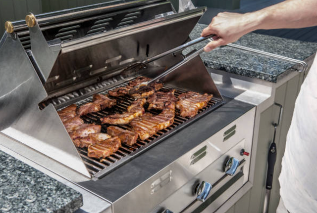 view of steaks cooking on a stainless steel grill, with tongs reaching in to flip a steak