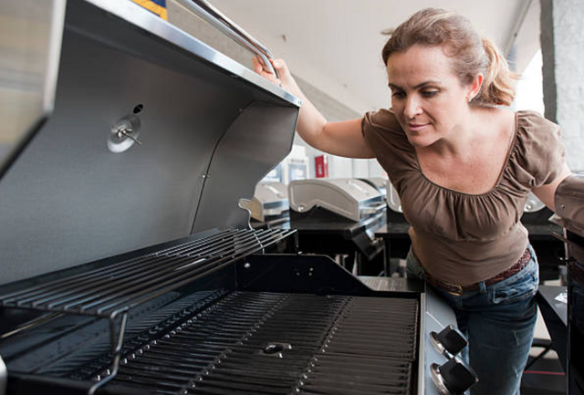 view of a woman looking into a stainless steel grill in an appliance store