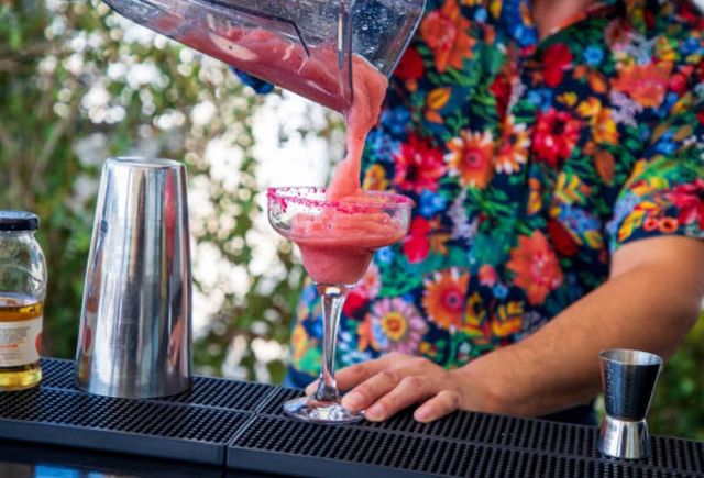 front view of a man pouring a blended red drink from a blender into a margarita glass