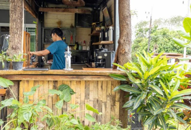 side view of a person working behind a rustic bar counter with a natural wood design and bar items around