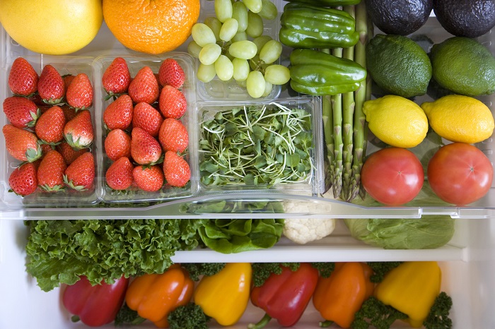 Crisper drawer of fridge filled with fruits and vegetables.