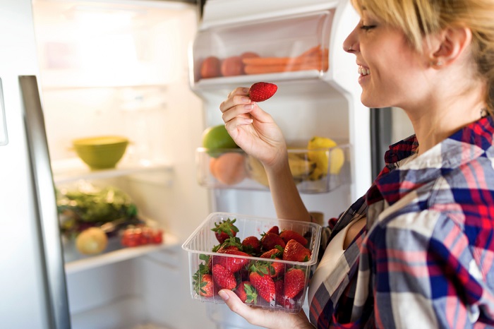 Young woman pulling strawberries out of the fridge.