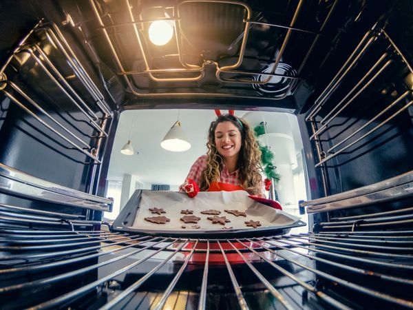 A smiling woman inserting holiday cookies into an oven 