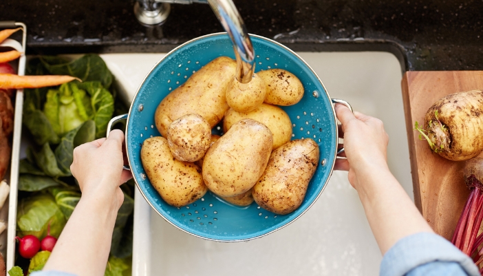 Closeup of someone rinsing off potatoes in a colander bowl