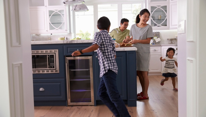 Two children rush around a kitchen while a mother and father prepare a meal.