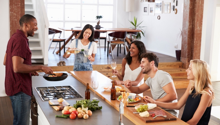 A man cooks dinner for his friends in a large, bright kitchen.