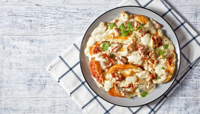 A bowl of creamy chicken sits on a gingham napkin and a white table.