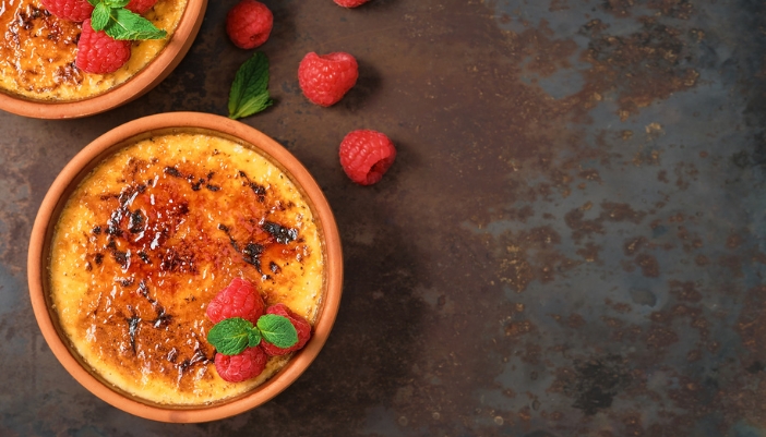 A creme brulee with berries rests on a black background.