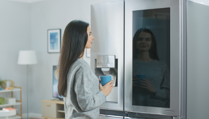 A woman drinks coffee and looks at her smart refrigerator grocery list.