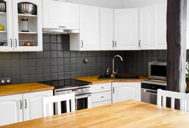 front view of a modern home kitchen with a black backsplash and white cabinets, wood countertops and stainless steel applianaces