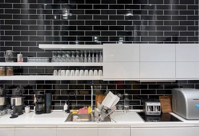 front view of a modern kitchen with black subwasy tile backsplash and white cabinets, with glasses and cups on them