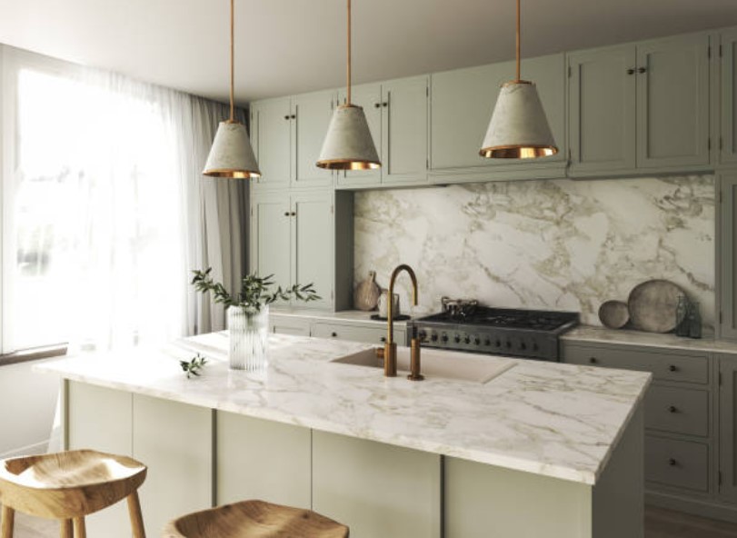 front view of a modern white and gold kitchen with three pendant lights over a marble island
