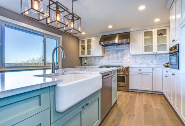 close view of a modern farmhouse kitchen with light blue cabinets, a large white sink, and light brown floors