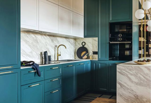 angled view of a trendy kitchen with teal and white cabinets, a double wall oven, and gold accents