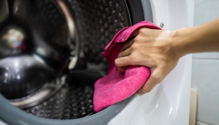 Hand wiping down washer with pink microfiber cloth