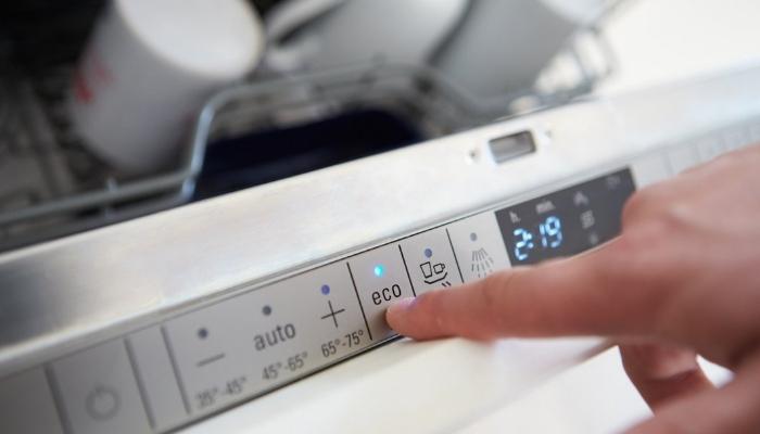 Finger pressing the Eco button on a dishwasher