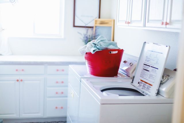 side view of a top load washer with a red basket of clothes on top of the dryer beside it
