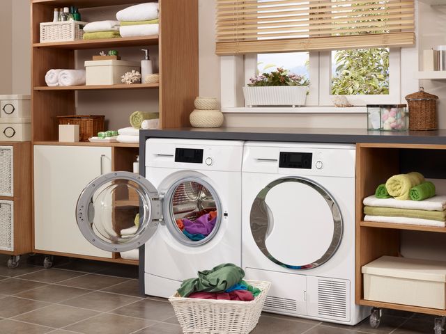 front view of a steam washer and dryer with the washer opened and a basket of colorful clothes in front