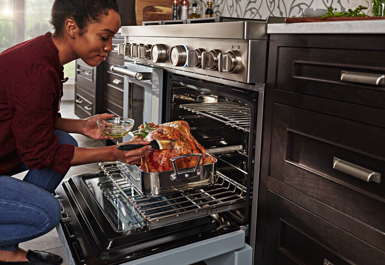African American woman basting turkey in duel fuel range oven