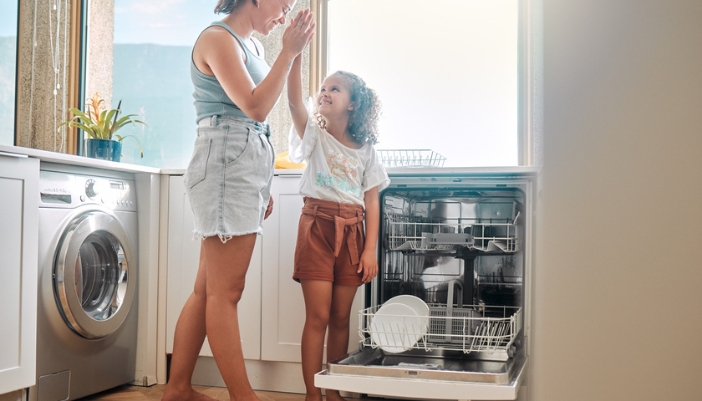 A child and her mother fill a dishwasher together.