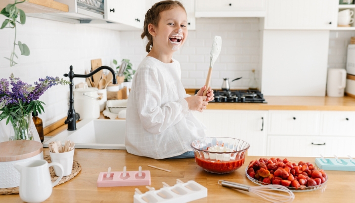 A young girl sits on a counter and makes fresh fruit popsicles.