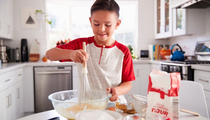 A young boy stirs flour and other ingredients in a bowl. 