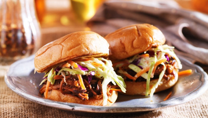 A pair of pulled pork sandwiches with coleslaw presented on a silver platter.