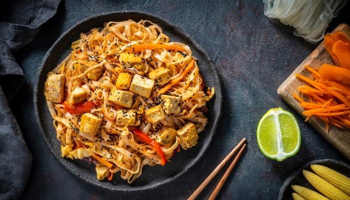 A black bowl filled with vegetarian Pad Thai surrounded by ingredients.