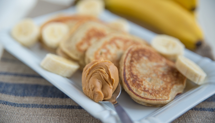 A stack of browned pancakes with peanut butter and banana slices on the plate. 
