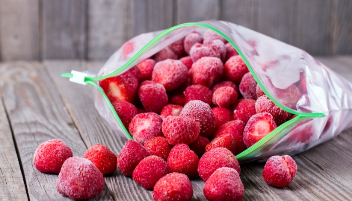 A large Ziploc bag of frozen strawberries spills onto a surface.