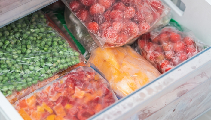An open freezer with several bags of frozen produce inside.