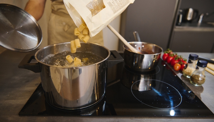 A pair of hands dumps circular noodles into boiling water.