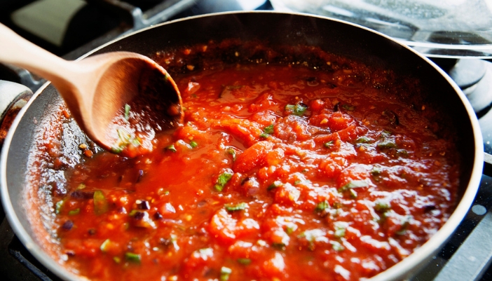 A wooden spoon stirs a pan of tomato sauce. 