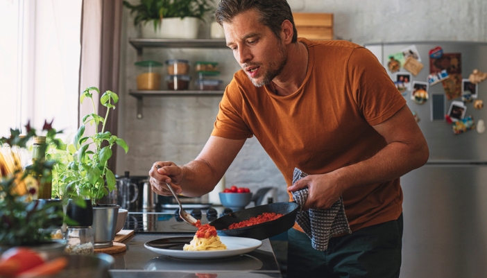 A man adds pasta sauce to a small pile of noodles.
