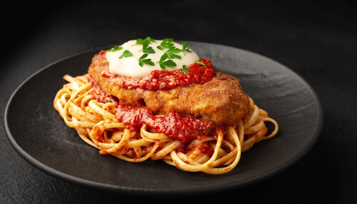 A black plate with noodles and chicken parmesan. 