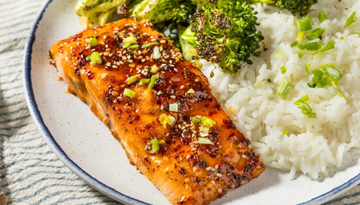 A plate with glazed salmon, rice, and veggies.